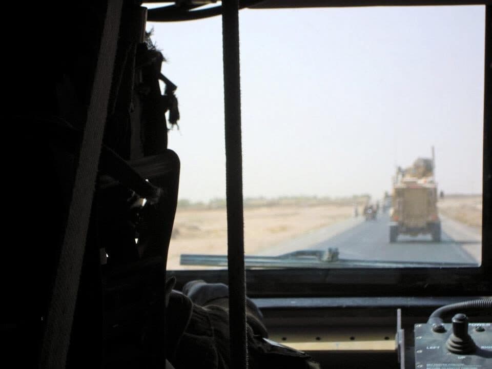Armored convoy moving down a desert road, seen through a vehicle windshield