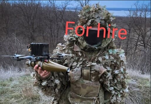 Drone operator in a ghillie suit holding an FPV attack drone, captioned "For hire"